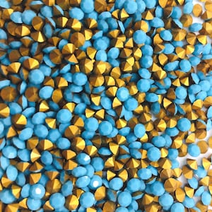 May include: A close-up of a collection of decorative gemstones. The gemstones are a mix of light blue and gold. The blue gemstones are round, while the gold ones have a faceted, triangular shape. Suitable for crafts or jewellery making.