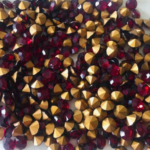 Puede incluir: Una colección de pedrería facetada roja y dorada. La pedrería roja es redonda y la dorada es triangular. La pedrería está dispersa por la superficie.