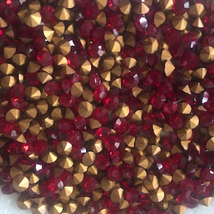 May include: A close-up view of a collection of red and gold rhinestones. The rhinestones are faceted, reflecting light, and are arranged closely together. The gold portion of the rhinestones has a metallic finish.