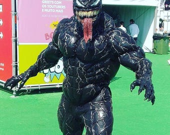 May include: A full-body Venom costume featuring a black, muscular suit with white vein-like patterns, a detailed mask with large white eyes, sharp yellow teeth, and a long, protruding red tongue. The suit covers the entire body with clawed hands.