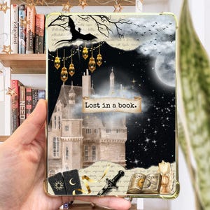 May include: A phone case with a dark background featuring a castle, stars, and the text "Lost in a book."