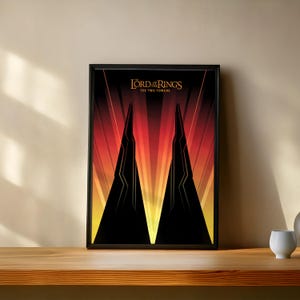 Può includere: Poster incorniciato con una grafica stilizzata de "Il Signore degli Anelli: Le Due Torri". L'opera raffigura due torri nere angolari su uno sfondo di linee rosse, arancioni e gialle. Il titolo è in lettere dorate.