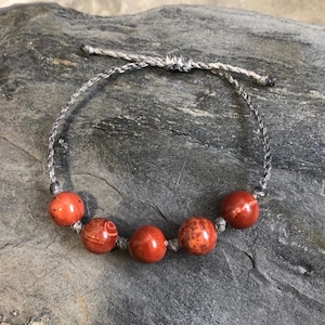 Peut inclure: Un bracelet en pierre rouge avec cinq perles rondes sur un cordon gris.