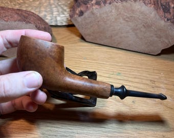 May include: A brown wooden pipe with a black stem and a black mouthpiece. The pipe is resting on a wooden surface.