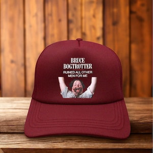May include: Maroon trucker hat with the text "BRUCE BOGTROTTER RUINED ALL OTHER MEN FOR ME" above an image of a person with their arms raised and mouth open.