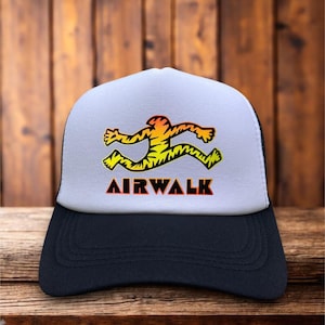 May include: A white and black trucker hat with a yellow, orange, and red tiger graphic and the text "AIRWALK" in red.