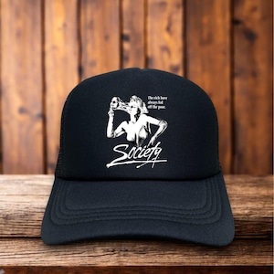 May include: Black trucker hat with a white graphic of a woman holding a mask, with the word "Society" in a stylized font. The text "The rich have always fed off the poor" is also included. The hat has a mesh back.