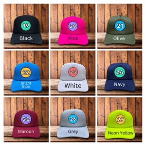 Puede incluir: Nueve gorras de b&eacute;isbol en varios colores, incluyendo negro, rosa, oliva, azul claro, blanco, azul marino, granate, gris y amarillo ne&oacute;n. Cada gorra tiene un n&uacute;mero y el nombre del color.