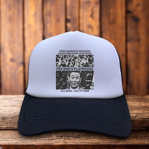 May include: A black and white trucker hat with a white front panel. The front features a graphic with the text "HERMAN WANTS REVENGE HARDCORE PUNK LIVE FROM PEE WEE'S PLAYHOUSE ALL AGES - JULY 17 1988". The hat has a black brim and mesh back.