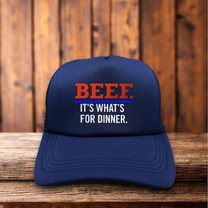 Pode incluir: Boné de caminhoneiro azul marinho com a palavra "BEEF" em letras vermelhas em bloco acima da frase "IT'S WHAT'S FOR DINNER" em branco. O boné tem uma parte traseira de malha preta e uma aba curva.