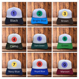Puede incluir: Se muestran nueve gorras de camionero en varios colores. Cada gorra tiene un panel frontal blanco, una visera de color y una parte trasera de malla negra. Los colores incluyen negro, azul brillante, marr&oacute;n, camuflaje, verde oscuro, verde, azul marino, azul real y granate.