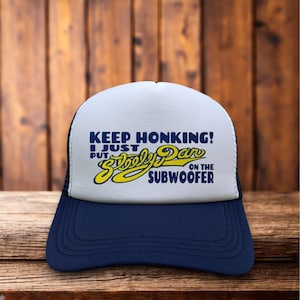 May include: A navy blue and white trucker hat with the text "KEEP HONKING! I JUST PUT Steely Dan ON THE SUBWOOFER" in blue and yellow. The hat has a mesh back and a curved brim.