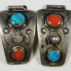May include: A pair of silver watch band buckles with turquoise and coral stones. The buckles are decorated with intricate designs.