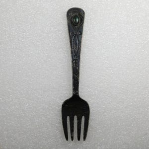 May include: A silver fork with an ornate design and a green stone at the top of the handle.