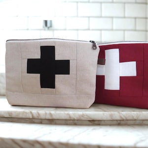 May include: Two zippered pouches made of fabric with a quilted design. One pouch is beige with a black cross, the other is red with a white cross.