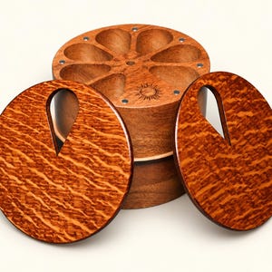 May include: A round wooden storage container with eight teardrop-shaped compartments and a sun icon engraving, accompanied by two circular wooden lids featuring a distinct wavy grain pattern and a single teardrop-shaped cutout in each.