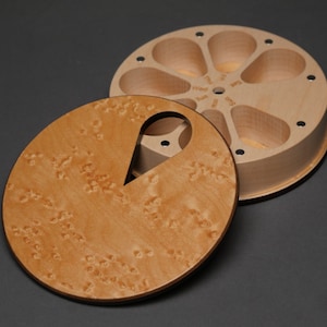 May include: A round wooden pill organizer with a removable lid featuring a textured burl wood grain pattern. The base contains seven petal-shaped compartments labeled with the days of the week, Sun, Mon, Tue, Wed, Thu, Fri, and Sat.