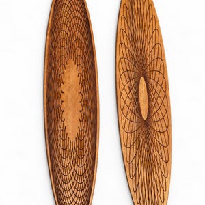 Op de afbeelding: Twee langwerpige ovale houten platen met ingewikkelde, donkerbruine lasergegraveerde geometrische patronen. De ontwerpen bestaan uit overlappende, concentrische elliptische lijnen die een complex, symmetrisch spirograafachtig visueel effect creëren.