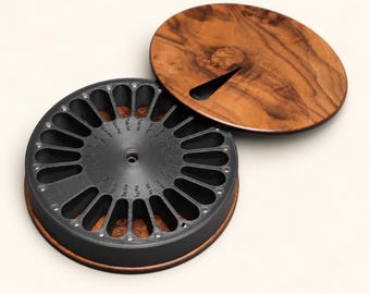 May include: A circular pill organizer with a dark gray interior featuring fourteen elongated slots arranged in a radial pattern. Each slot is labeled with days of the week and AM or PM indicators. A separate round wooden lid with a grain pattern.