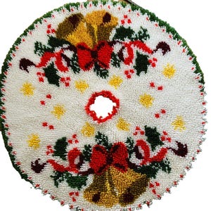 May include: A round, white, tufted Christmas tree skirt featuring a punch needle design of gold bells, red bows, and green holly leaves. The circular mat has a central opening with a red border and a green scalloped edge around the perimeter.