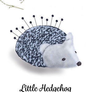 May include: A gray and white hedgehog pincushion with black pins sticking out of its back. The pincushion is sitting on a white background. The text "Little Hedgehog pincushion" is written below the pincushion.