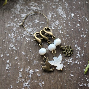 May include: A gold-toned charm bracelet with white beads and charms of a snowflake and two birds. The bracelet is on a brown wooden surface with white flakes.