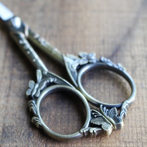 May include: Antique silver-toned scissors with ornate butterfly and floral designs. The scissors have a detailed, intricate design.