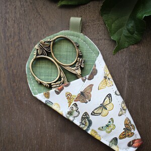 May include: A green fabric scissor case with a butterfly print and a pair of antique-style scissors with ornate handles.