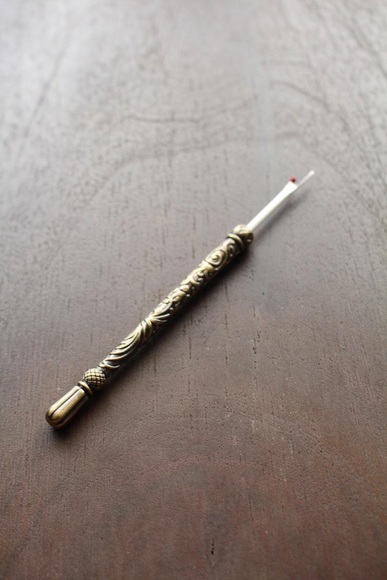 May include: A gold-colored thread cutter with an ornate handle. The cutter has a small red tip.