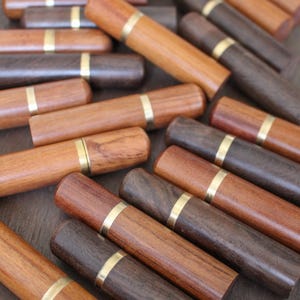 May include: A collection of wooden needle cases with gold trim. The cases are made of different types of wood, including dark and light wood.