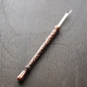 May include: A copper-colored crochet hook with an ornate handle and a white tip.