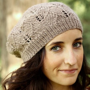 May include: A woman wearing a brown knitted hat with a lacy pattern. The hat is pulled down over her forehead and she is looking at the camera with a slight smile.