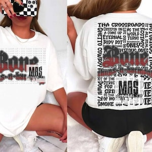 Puede incluir: Camiseta blanca con un estampado gráfico en negro y rojo de la palabra "Bone" y el texto "Things-n-Harmony" en la parte delantera. La parte posterior de la camiseta tiene un estampado gráfico en negro y rojo de la palabra "Bone" y una columna de texto que incluye "Ghetto Cowboy", "Notorious Thugs", "Tha Crossroads", "Creepin One", "A Come Up World", "Eternal Turns", "Body Rot", "Only", "Hteous Ones", "1st of the Month", "Stric", "For", "Gri", "Fo Tha", "Mod", "Smoke On", "No Surrenderer" y "999".