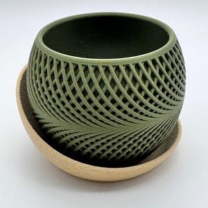 May include: A green ceramic planter with a geometric pattern and a matching saucer. The planter has a rounded shape and a wide opening.