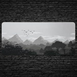 May include: A rectangular mouse pad featuring a grayscale landscape design. The image depicts mountains, trees, and clouds, with birds in flight. The color palette is limited to shades of gray and black.