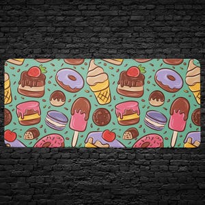 May include: A rectangular mat with a repeating pattern of colorful desserts on a teal background. The design includes donuts, ice cream cones, cakes, cookies, and popsicles. Sprinkles and other small details are scattered throughout the design.