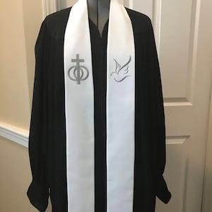 May include: White stole with silver embroidery of a cross with rings and a dove. The stole is worn over a black robe.