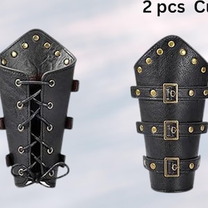 Peut inclure: Deux brassards en cuir noir avec des accents dor&eacute;s. Un brassard a un design &agrave; lacets et l'autre a trois sangles &agrave; boucle.
