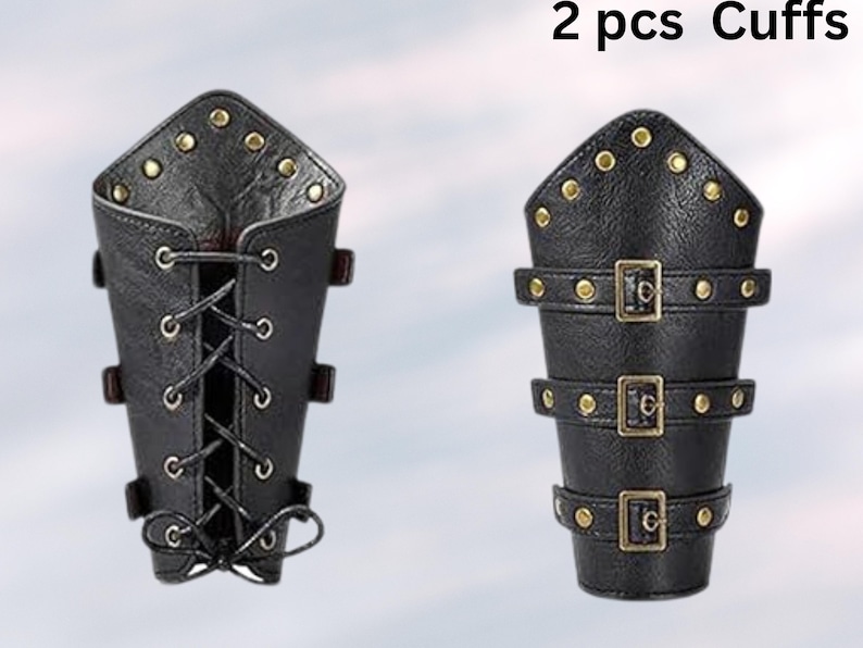 Peut inclure: Deux brassards en cuir noir avec des accents dor&eacute;s. Un brassard a un design &agrave; lacets et l'autre a trois sangles &agrave; boucle.