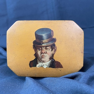 May include: A wooden box with a painted image of a man wearing a blue top hat and a white shirt. The box has a yellow background.