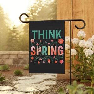 May include: A black garden flag with the text "Think Spring" in colorful letters surrounded by floral designs.