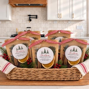 May include: Four clear pouches of Christmas simmer potpourri in a woven basket. Each pouch contains dried orange slices, cinnamon sticks, and pine needles, topped with a red and white gingham ribbon and a round label with tree graphics.
