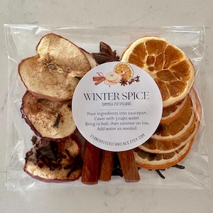 May include: A clear plastic bag containing dried apple slices, orange slices, cinnamon sticks, and star anise. A circular white label reads: WINTER SPICE SIMMER POTPOURRI. Pour ingredients into saucepan. Cover with 3 cups water. Bring to boil, then simmer on low. Add water as needed. STONEHOUSEBOTANICALS.ETSY.COM.