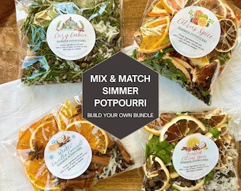 May include: Four clear plastic bags filled with dried simmer potpourri ingredients. The labels read Cozy Cabin, Citrus Spice, Winter Vanilla Coconut, and Frosted Citrus Spice. A central dark gray graphic displays the text MIX & MATCH SIMMER POTPOURRI BUILD YOUR OWN BUNDLE.