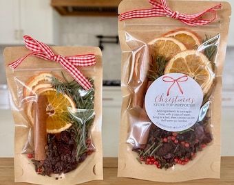 May include: Two clear pouches with kraft paper backing containing stove top potpourri. Each pouch features dried orange slices, cinnamon sticks, rosemary, cranberries, and red peppercorns, tied with a red and white gingham ribbon.