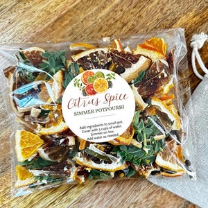 May include: A clear plastic bag containing dried citrus slices, green herbs, and spices. A circular white label features the text Citrus Spice SIMMER POTPOURRI and instructions: Add ingredients to small pot. Cover with 3 cups of water. Simmer on low. Add water as needed.
