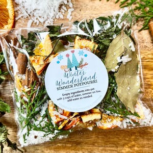 May include: A clear plastic bag filled with dried botanicals for simmering. The bag contains orange slices, cinnamon sticks, bay leaves, and other herbs. A round label reads "Winter Wonderland Simmer Potpourri".