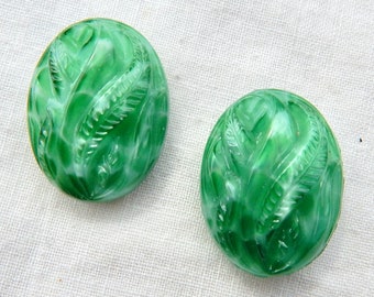 Puede incluir: Un par de botones de vidrio verde con un diseño de hojas talladas. Los botones son redondos y tienen un acabado brillante.