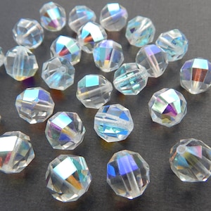 May include: A collection of iridescent clear glass beads with a faceted design. The beads are round and have a rainbow sheen.