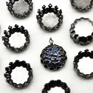 Peut inclure: Gros plan sur dix montures métalliques argentées pour cabochons. Les montures ont un bord festonné et un intérieur rond et lisse. Une monture a un cabochon noir iridescent.